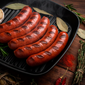 Chorizos a la brasa con marcas de parrilla sobre plancha de hierro, acompañados de hierbas y especias.