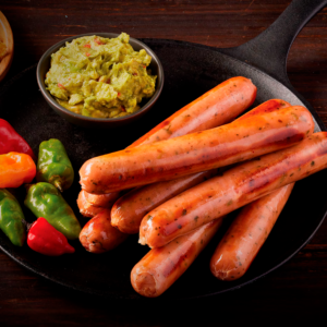Chorizos mexicanos en sartén de hierro con guacamole fresco y ajíes coloridos.