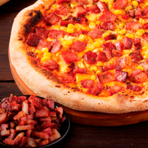 Tocineta cubicada sobre pizza con maíz y queso, junto a bowl con cubos de tocineta frita.