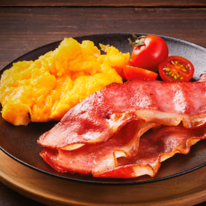 Tocineta premium frita con huevos revueltos y tomates cherry en plato negro.